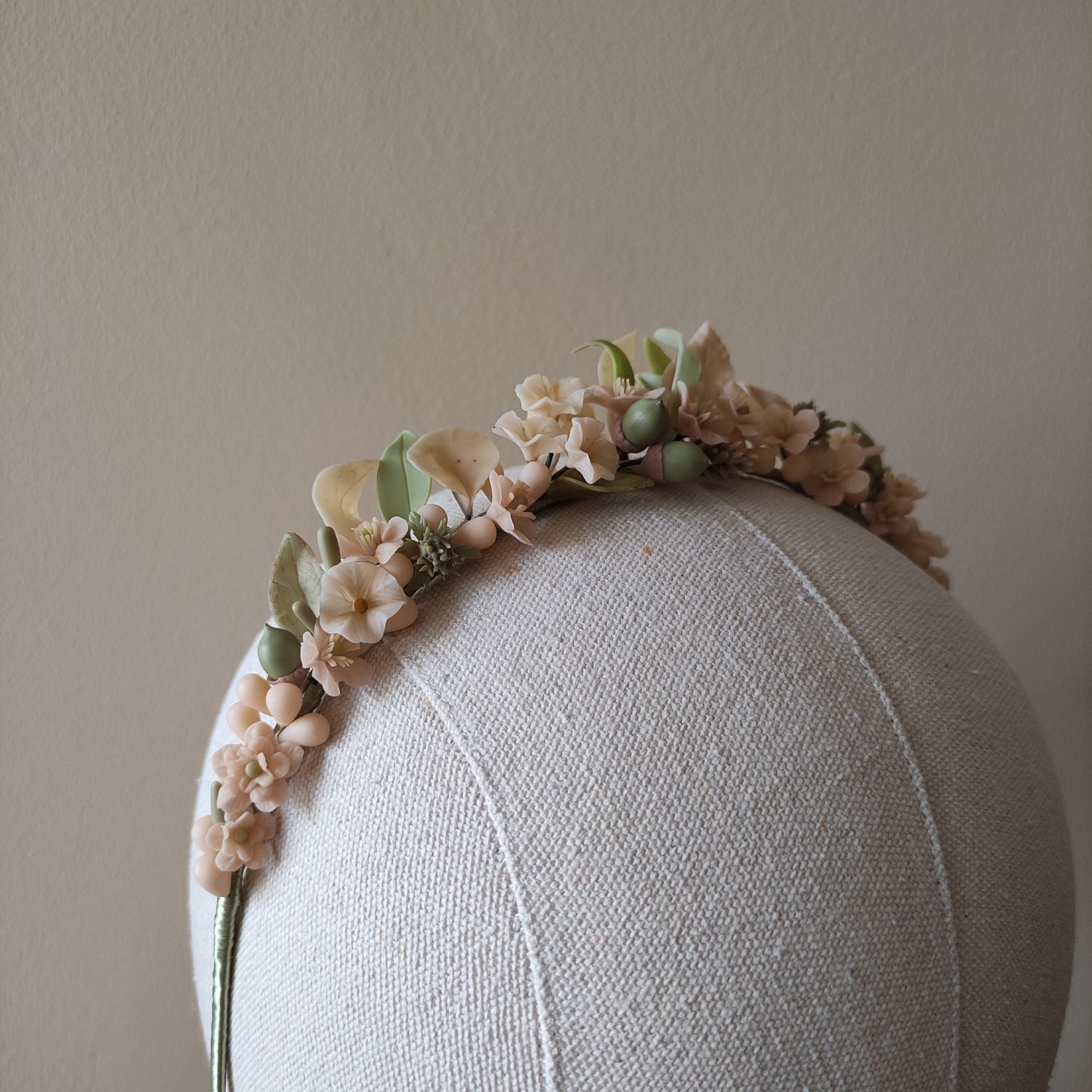 diadema dehesa Detailed view of a Dehesa-style floral headpiece made of cold porcelain. This botanical accessory features intricate hand-sculpted flowers and acorns, elegantly mounted on a silk-wrapped metal band
